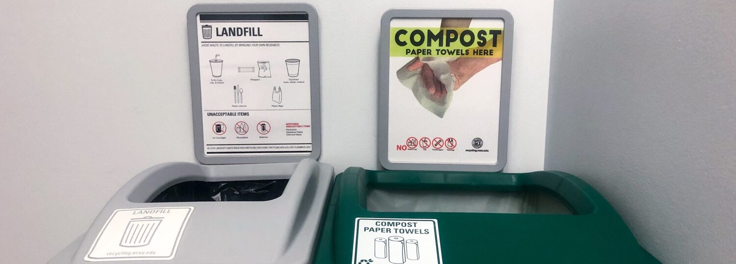 A photo of two bins placed next to each other in the corner of a Wilson College of Textiles bathroom. One is a waste bin and is gray. One (right) is a green bin and is for composting. Both have signage above them explaining what items to place in each type of bin.